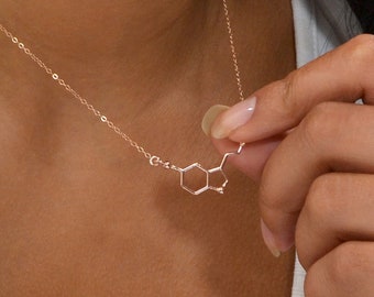 May include: A rose gold necklace featuring a serotonin molecule pendant on a delicate chain. The pendant is a chemical structure design. The text on the image states: Material - Rose Gold, Length - 16 inches (See listing to measure your size).