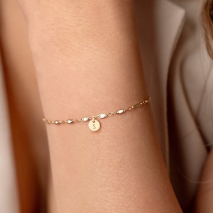Könnte beinhalten: Ein zartes goldenes Kettenarmband mit einem kleinen, runden Anhänger mit dem Buchstaben 'S'. Das Armband ist aus 14 Karat Gold gefüllt.