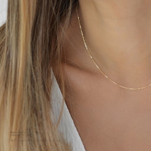 May include: A delicate gold-filled necklace with a fine chain is draped around a person's neck. The necklace is a simple, elegant design, perfect for layering or wearing alone. The chain is approximately 16 inches long.