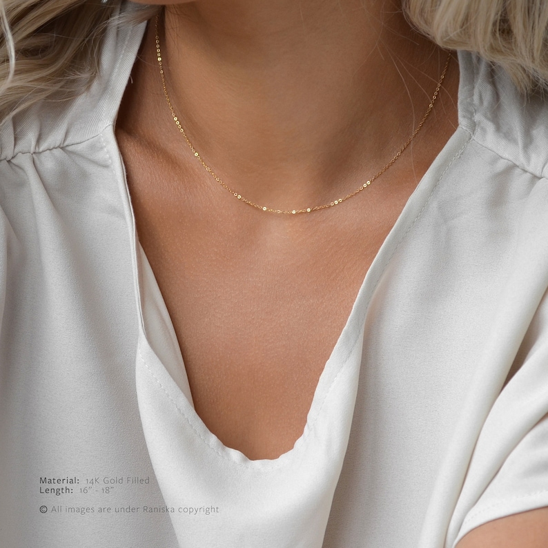 May include: Delicate gold-filled necklace with small, evenly spaced circular charms. The necklace is shown against a white blouse. The length is between 16 and 18 inches. The material is 14K gold filled.