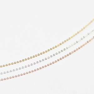 May include: Three delicate chain necklaces in gold, silver, and rose gold tones. The chains are thin and feature small, circular links. The necklaces are displayed against a white background, highlighting their colors and textures. Ideal for layering or wearing alone.