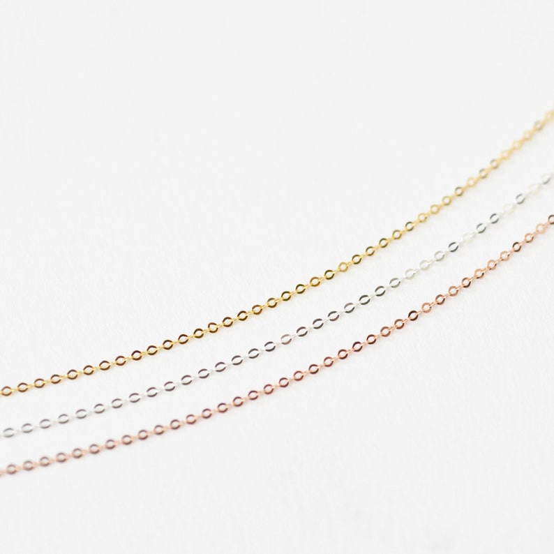 May include: Three delicate chain necklaces in gold, silver, and rose gold tones. The chains are thin and feature small, circular links. The necklaces are displayed against a white background, highlighting their colors and textures. Ideal for layering or wearing alone.