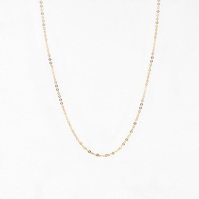 May include: A delicate gold-colored chain necklace. The necklace features small, evenly spaced links that create a subtle, elegant design. The chain is displayed against a plain white background, highlighting its simple beauty.