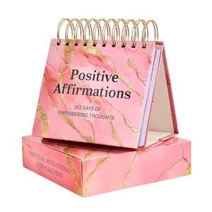 Op de afbeelding: Een roze bureaukalender met marmerpatroon en gouden accenten. De kalender heeft een gouden spiraalbinding. De tekst op de kalender luidt "Positive Affirmations" en "365 Days of Empowering Thoughts". De doos leest "Perpetual Motivational Daily Calendar".