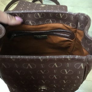 K&ouml;nnte beinhalten: Eine braune Ledertasche mit einem goldenen Verschluss und einem braunen und wei&szlig;en Muster. Die Tasche hat eine Rei&szlig;verschlusstasche im Inneren.