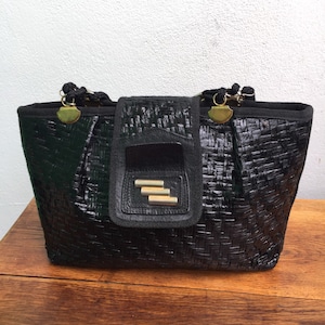 Peut inclure: Sac fourre-tout en cuir noir tissé avec des ferrures dorées et une fermeture à rabat. Le sac a un motif tissé et une petite poche sur le devant.