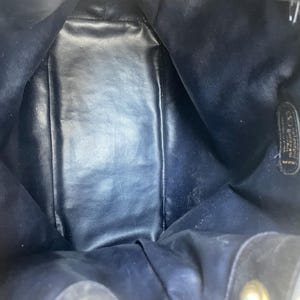 May include: Interior view of a dark blue leather handbag. The bag's interior is visible, showing a spacious compartment. The leather appears to be slightly worn, with some areas showing wear and tear. The bag has a drawstring closure.