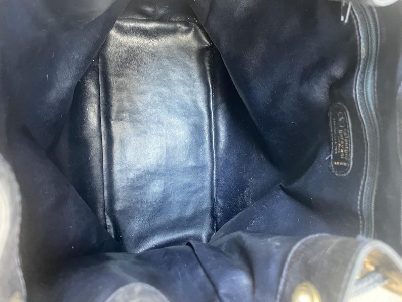 May include: Interior view of a dark blue leather handbag. The bag's interior is visible, showing a spacious compartment. The leather appears to be slightly worn, with some areas showing wear and tear. The bag has a drawstring closure.