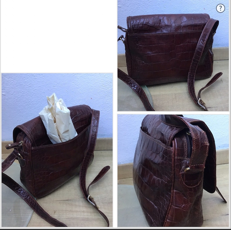 Op de afbeelding: Bruine leren crossbodytas met krokodillenleertextuur. De tas heeft een klepsluiting, een lange verstelbare riem en een ritsvak aan de achterkant. De binnenkant is gevoerd met lichtgekleurde stof. De tas wordt vanuit meerdere hoeken getoond.