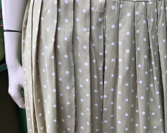 May include: A pleated skirt in a light olive green color, adorned with a pattern of white polka dots. The skirt is displayed on a mannequin, showcasing its design and fabric texture. The skirt's pleats create a flowing silhouette.
