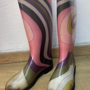Op de afbeelding: Een paar kniehoge rubberen regenlaarzen met een semi-transparante afwerking en een wervelend, meerkleurig grafisch patroon in tinten roze, olijfgroen, paars en crème, compleet met effen zwarte zolen en een ontwerp met een ronde neus.