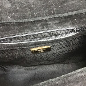 May include: Black suede handbag with a zippered closure. The interior features a patterned lining and a gold-toned label. The bag's design is simple and elegant, suitable for various occasions.