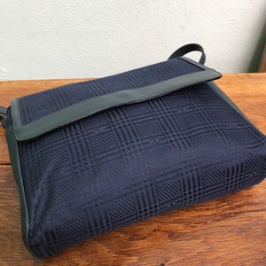 May include: A navy blue shoulder bag with a flap closure. The bag features a plaid pattern and dark blue leather trim. The bag has a shoulder strap and is made of a woven fabric.