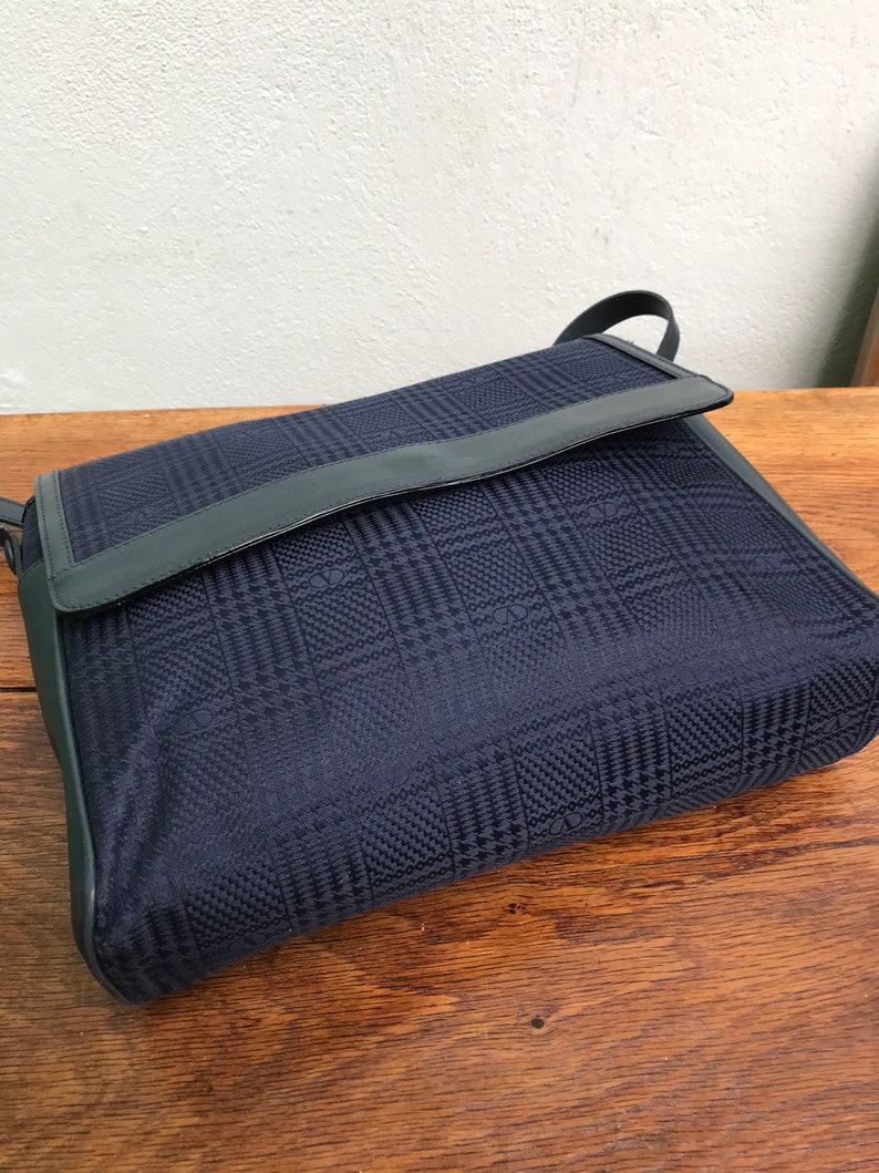 May include: A navy blue shoulder bag with a flap closure. The bag features a plaid pattern and dark blue leather trim. The bag has a shoulder strap and is made of a woven fabric.
