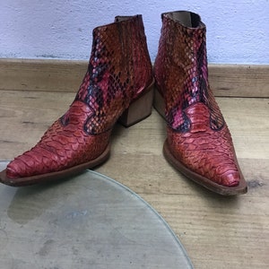 Puede incluir: Un par de botines de tobillo de piel de serpiente roja y marrón con punta puntiaguda y tacón de bloque.