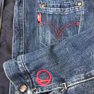 Peut inclure: Une veste en jean bleu avec un logo brod&eacute; rouge sur la manche et un patch Levi's rouge sur la poche.