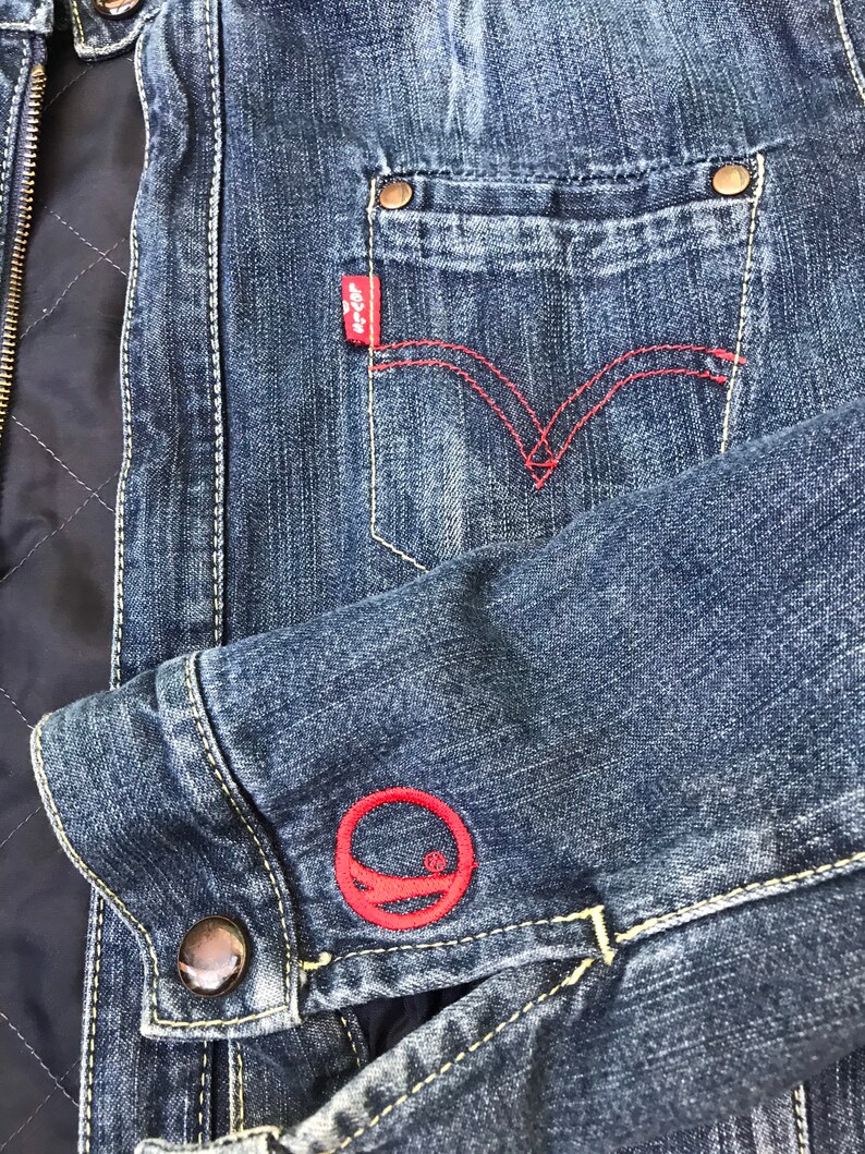 Peut inclure: Une veste en jean bleu avec un logo brod&eacute; rouge sur la manche et un patch Levi's rouge sur la poche.