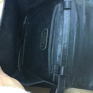 May include: Black leather handbag with an open interior, featuring a zippered pocket and a strap. The interior displays a label with the brand name "Valentino Garavani" and "Genuine Leather Made in Italy".