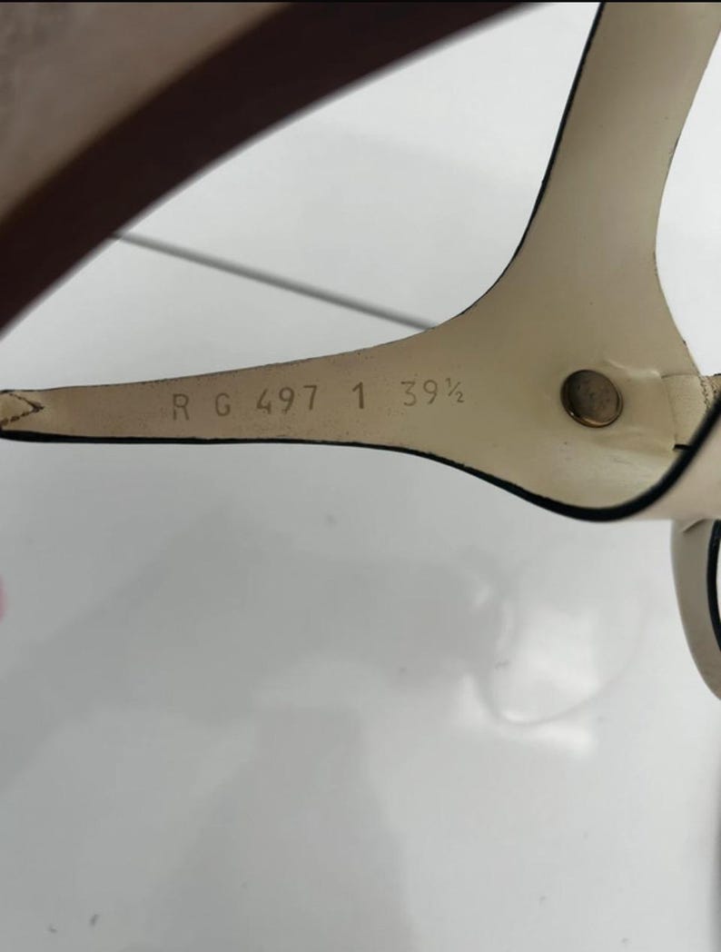 May include: Close-up of a cream-colored sandal strap with a dark brown sole. The strap has the text "R G 497 1 39 1/2" printed on it. The sandal is likely a size 8.5 US.