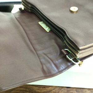 May include: A brown leather handbag with a gold-colored clasp and a gold-colored logo. The bag is open, revealing the interior and layered design. The bag has a magnetic closure.