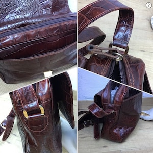 Op de afbeelding: Bruine leren handtas met een krokodillenleer textuur. De tas heeft een handvat aan de bovenkant en een schouderriem. Het heeft een hoofdvak met ritssluiting, een voorvak en goudkleurige hardware. De tas is rechthoekig en heeft een klepsluiting.