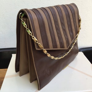 May include: A brown and tan leather handbag with a gold chain strap. The flap features vertical pleats, and the bag has a gold chain strap. The Valentino logo is embossed on the front.