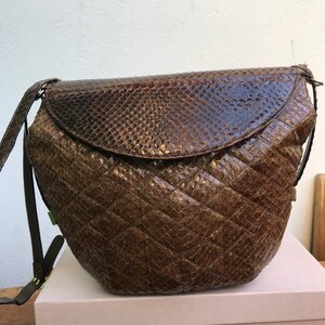 Peut inclure: Un sac à bandoulière en peau de serpent marron avec un motif matelassé en losanges sur le corps et un rabat incurvé lisse. Le sac présente une longue bandoulière fine assortie avec une boucle en métal pour le réglage et une forme arrondie.