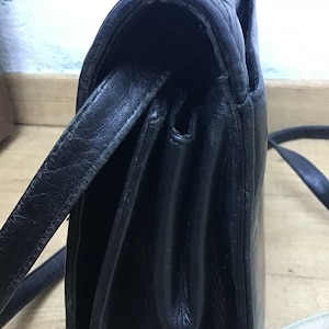 May include: Black leather shoulder bag with a quilted flap and a long strap. The bag has a rectangular shape and appears to be vintage. The leather shows signs of wear, adding to its character. The bag is designed to be worn over the shoulder.