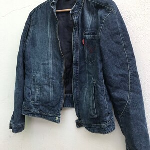 Peut inclure: Une veste en jean bleu fonc&eacute; avec une fermeture &eacute;clair et un logo rouge sur la poche poitrine.