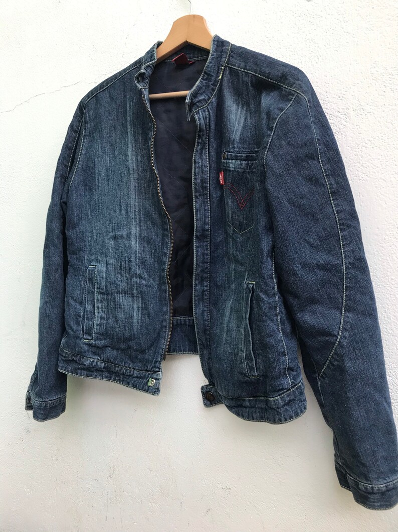 Peut inclure: Une veste en jean bleu fonc&eacute; avec une fermeture &eacute;clair et un logo rouge sur la poche poitrine.