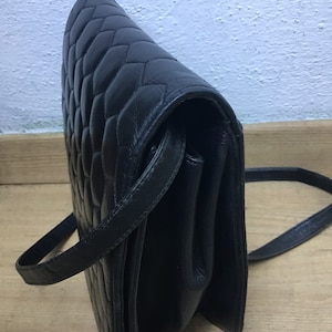 May include: Black quilted leather crossbody bag with a long strap. The bag features a diamond pattern and a flap closure. The bag is made of a smooth, shiny leather material.