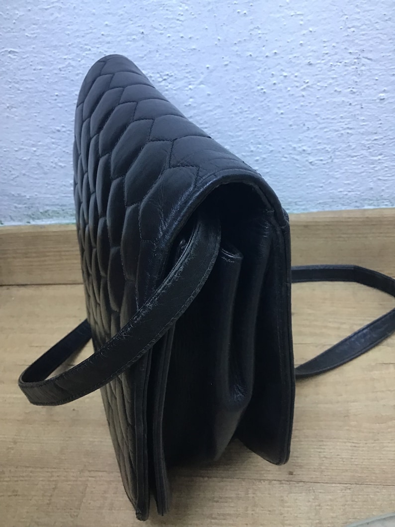 May include: Black quilted leather crossbody bag with a long strap. The bag features a diamond pattern and a flap closure. The bag is made of a smooth, shiny leather material.