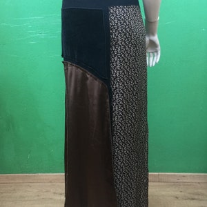Op de afbeelding: Een enkellange rok met een patchworkontwerp, voorzien van een effen zwarte tailleband, een zwart paneel, een bruin satijnachtig paneel en een zwart stoffen paneel met een kleine witte bloemenprint. De rok heeft een recht silhouet en naden.