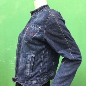 Peut inclure: Une veste en jean bleu fonc&eacute; avec un col montant et un d&eacute;tail de couture rouge sur la poche poitrine gauche.