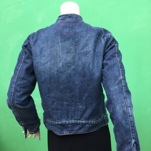 Peut inclure: Une veste en jean bleu avec un petit patch carr&eacute; au dos. La veste a des manches longues et une fermeture &agrave; boutons.