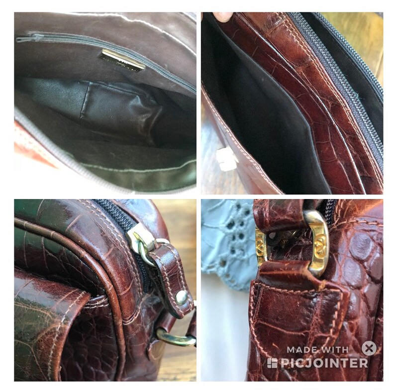 Op de afbeelding: Een bruine leren handtas met een krokodillenstructuur. De tas heeft een ritssluiting, een goudkleurige gesp en een donker interieur. De tas lijkt vintage te zijn.
