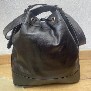 May include: Black leather bucket bag with a drawstring closure and shoulder strap. The bag has a rounded base and gold-toned hardware. The leather has a textured appearance.