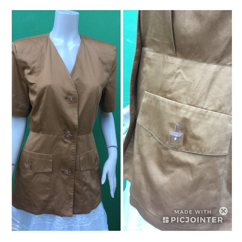 May include: A tan-coloured jacket with short sleeves, a V-neck, and three decorative buttons. It has two front pockets and a fitted waist. The right side shows a close-up of a pocket with a decorative button.