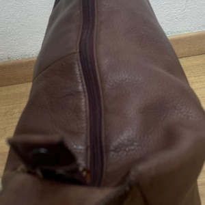 May include: A brown leather shoulder bag with a zipper closure. The bag has a flap with a buckle. The leather has a textured appearance. The bag is designed to be worn over the shoulder.