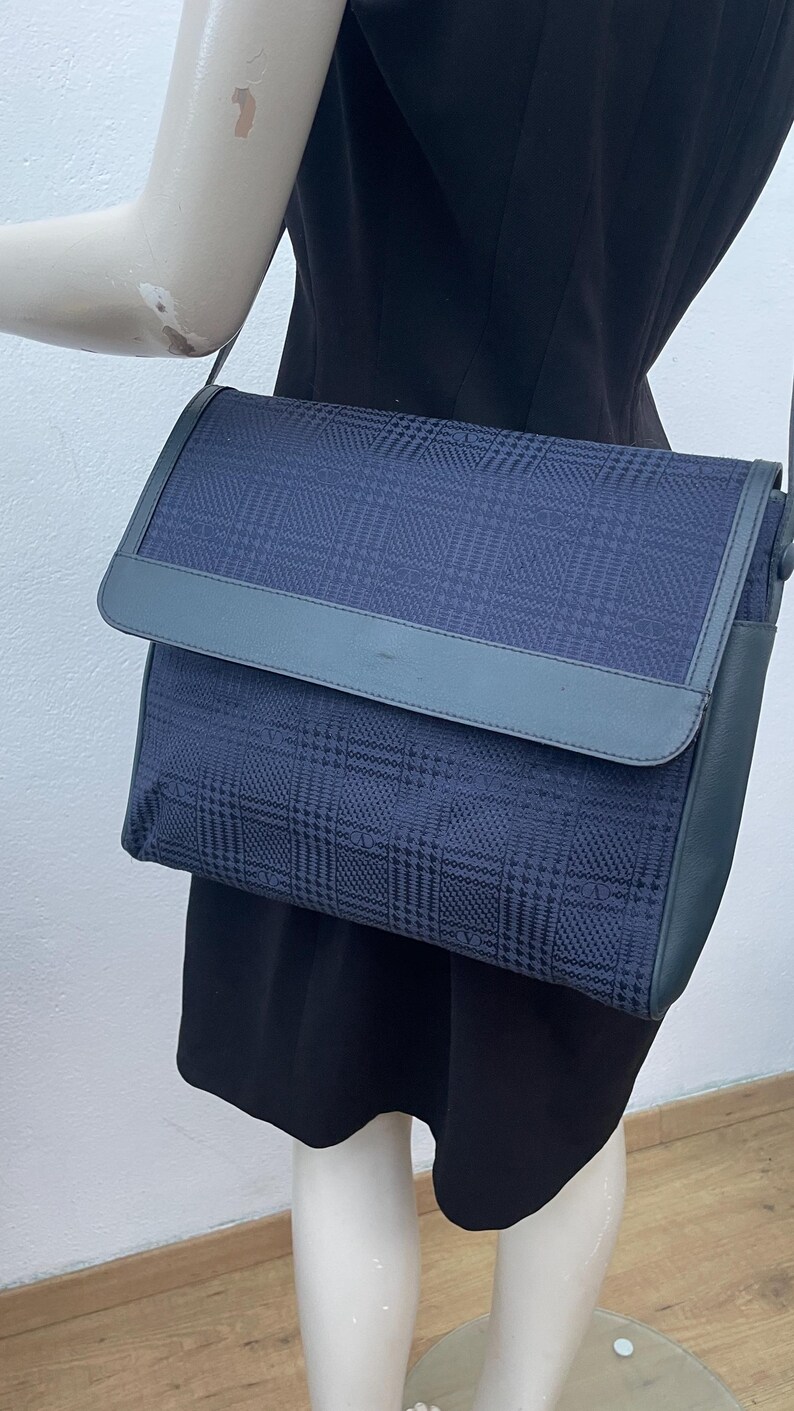 May include: A navy blue crossbody bag with a plaid pattern. The bag features a flap closure and a matching shoulder strap. The bag is made of a textured fabric and has a leather trim.