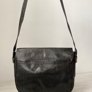 May include: Black leather shoulder bag with a snakeskin pattern. The bag has a flap closure and a long adjustable strap.