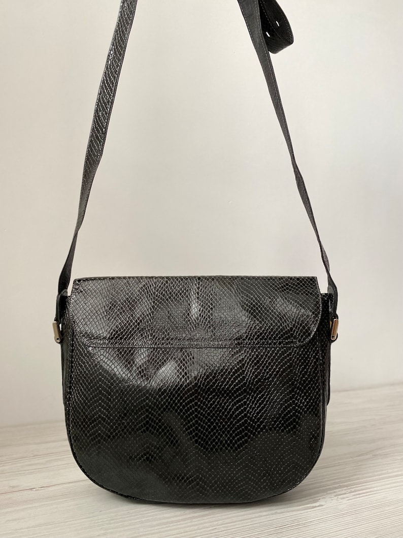 May include: Black leather shoulder bag with a snakeskin pattern. The bag has a flap closure and a long adjustable strap.