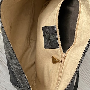 May include: The inside of a black leather handbag with a zippered pocket and a gold-colored metal tag that reads "Made in Italy" and "Murano Venice".