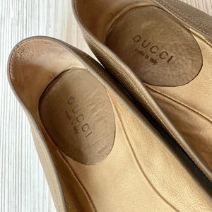 K&ouml;nnte beinhalten: Ein Paar beigefarbene Gucci-Ballerinas mit dem Text "Gucci made in Italy" auf der Innensohle.