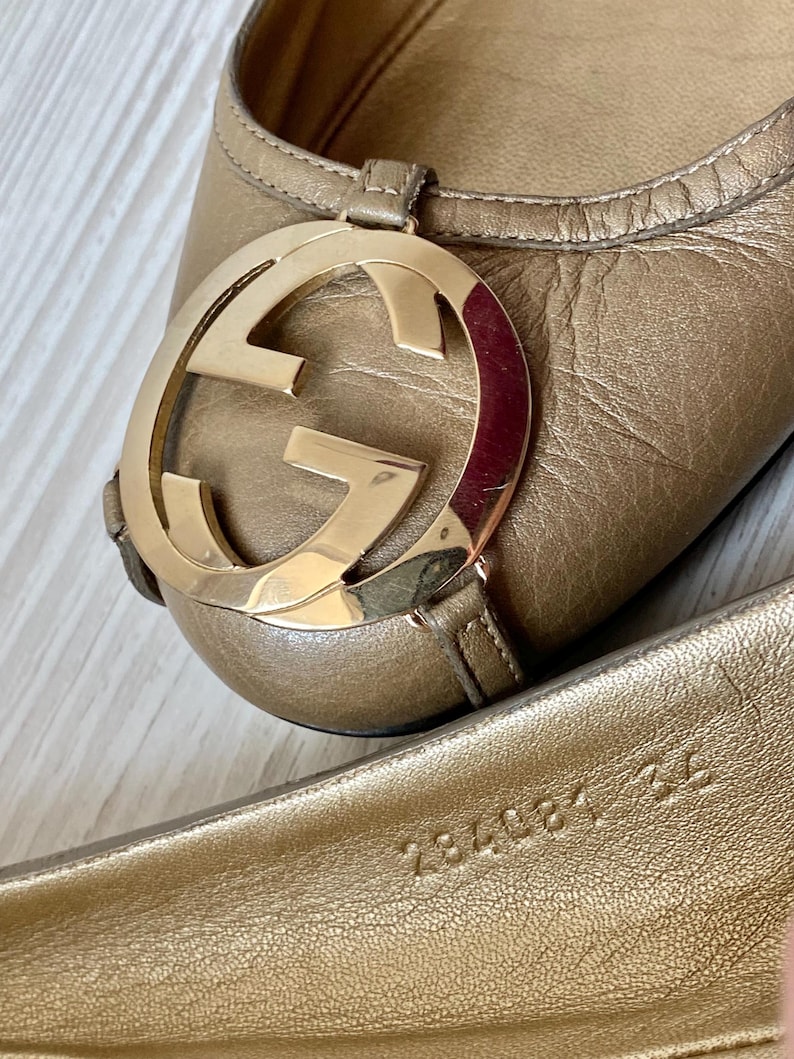 K&ouml;nnte beinhalten: Ein Paar goldene Ballerinas aus Leder mit einem gro&szlig;en, goldenen, ineinandergreifenden GG-Logo an der Spitze. Die Ballerinas haben ein Gr&ouml;&szlig;enetikett auf der Innensohle mit der Aufschrift "234081 422".