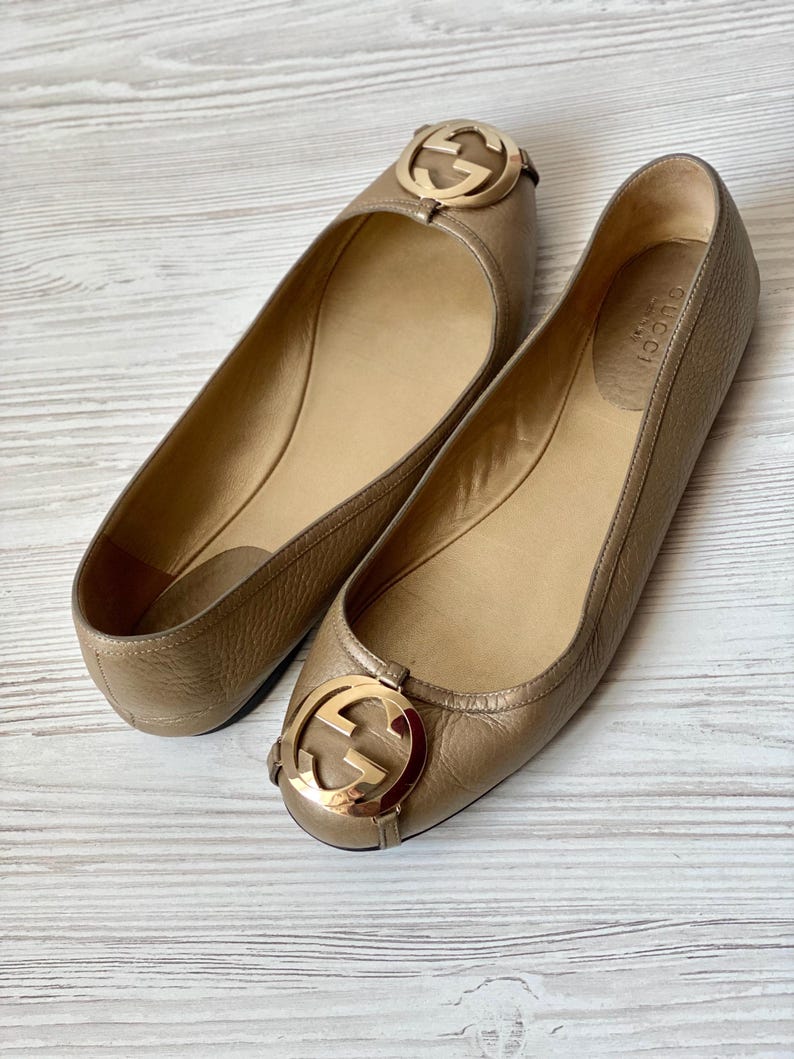 K&ouml;nnte beinhalten: Ein Paar braune Gucci Ballerinas aus Leder mit goldenen, ineinandergreifenden G-Logo-Akzenten.