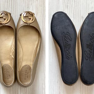 K&ouml;nnte beinhalten: Ein Paar goldfarbene Gucci Ballerinas mit einem goldenen, ineinandergreifenden G-Logo an der Spitze. Die Ballerinas sind aus Leder und haben eine spitze Zehenpartie. Die Ballerinas befinden sich auf einem wei&szlig;en Hintergrund.