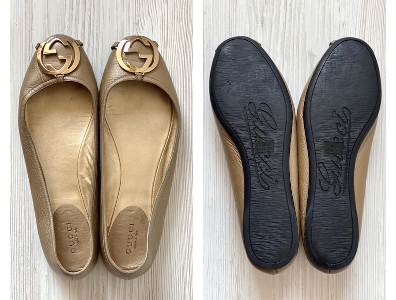 K&ouml;nnte beinhalten: Ein Paar goldfarbene Gucci Ballerinas mit einem goldenen, ineinandergreifenden G-Logo an der Spitze. Die Ballerinas sind aus Leder und haben eine spitze Zehenpartie. Die Ballerinas befinden sich auf einem wei&szlig;en Hintergrund.