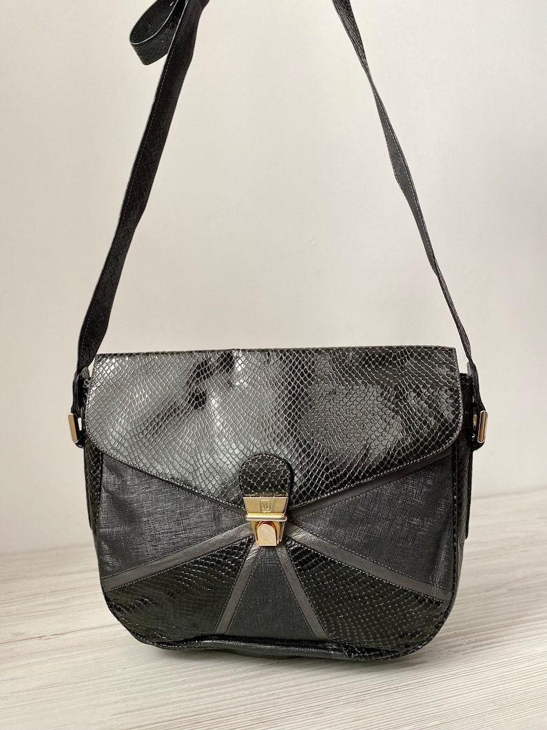 May include: A black leather shoulder bag with a snakeskin pattern and a gold clasp. The bag has a flap closure and a long adjustable strap.