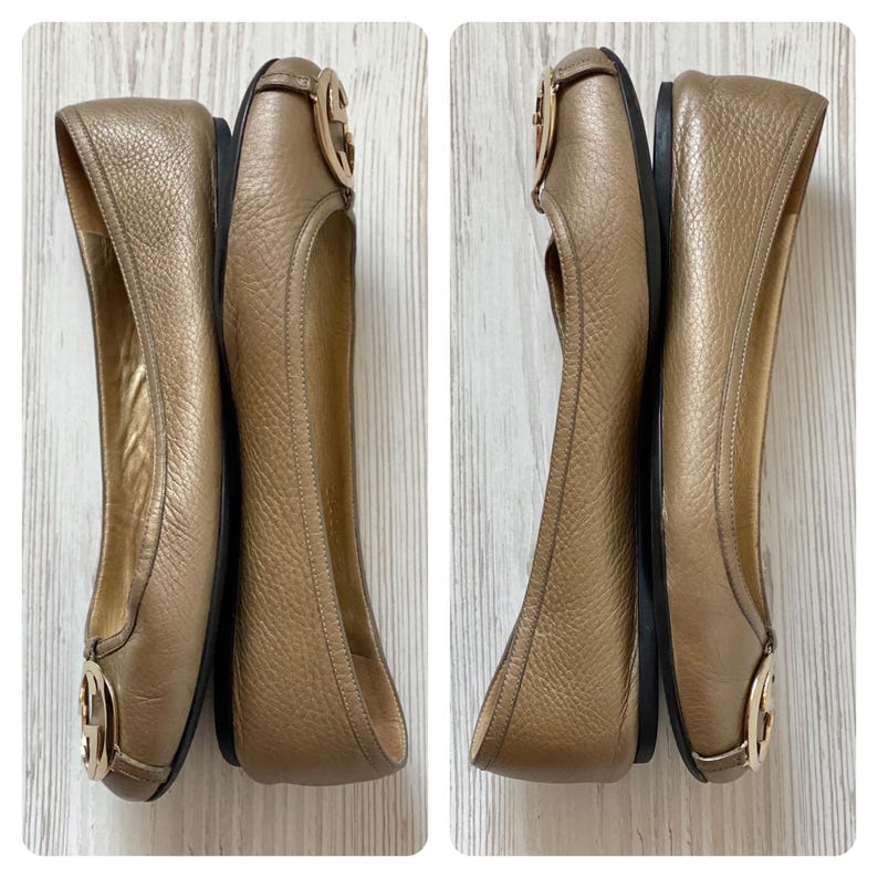 K&ouml;nnte beinhalten: Ein Paar goldene Ballerinas aus Leder mit einem goldenen, ineinander verschlungenen G-Logo an der Spitze. Die Ballerinas befinden sich auf einer wei&szlig;en Oberfl&auml;che.